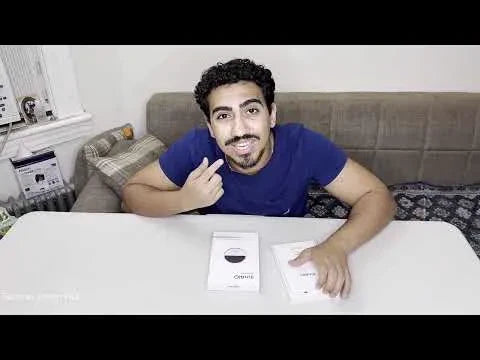 Smiling bearded man in a blue shirt pointing at two white booklets on a table.