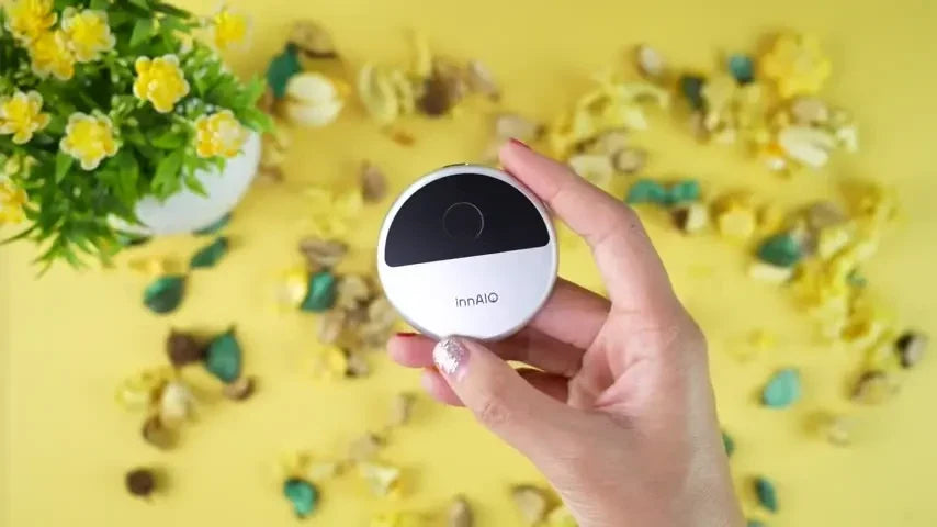 Hand holding small white InnAIO translator device above yellow petals